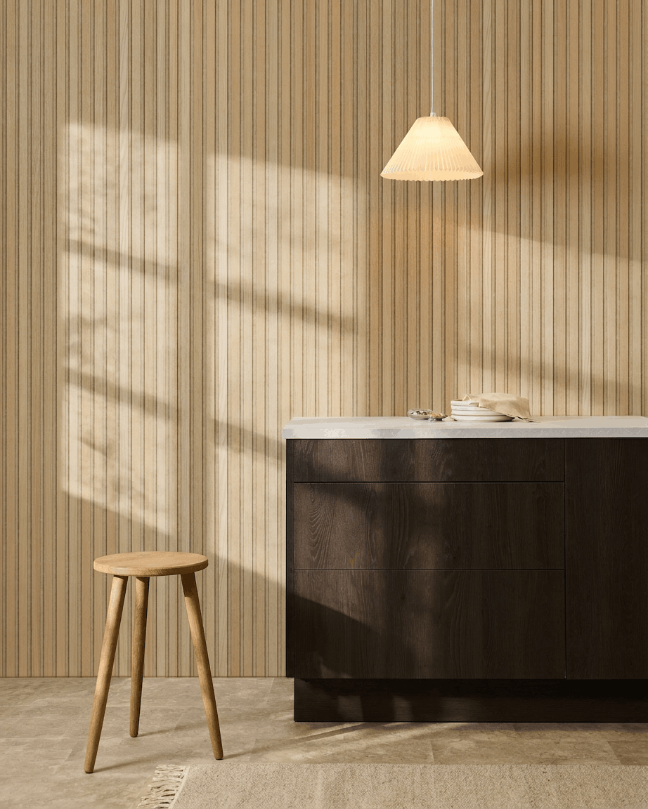 Scandinavian kitchen featuring WoodUpp Akupanel Classic Oak acoustic slatwall panel, dark wood cabinets, wooden stool, pendant light, and sunlight casting shadows.